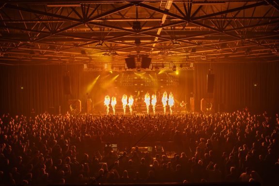 Konzert mit einer großen Menschenmenge und intensiven Feuereffekten auf der Bühne.